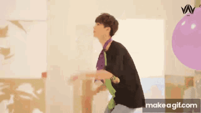 a young man is standing in front of a purple balloon .