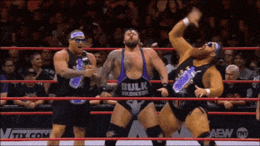 three men in a wrestling ring one of whom is wearing a bulk bronson tank top
