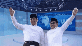 two men standing in front of a news screen with their arms in the air