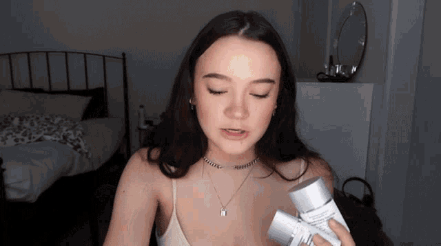 a woman in a white tank top holds two bottles of lotion