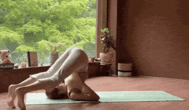 a woman is doing a yoga pose in front of a window with a mccallister book on the window sill