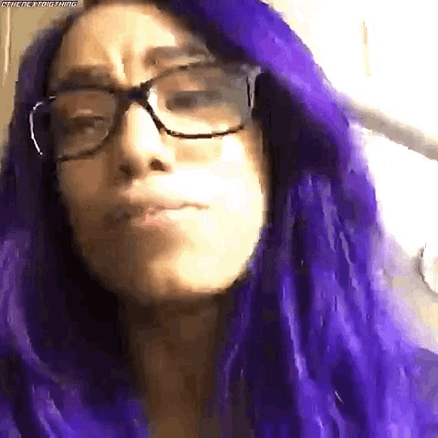 a woman with purple hair and glasses making a face .