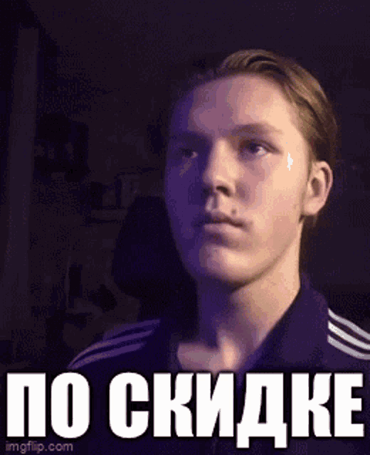 a young man in a purple shirt is looking at the camera with a foreign language sticker on his face .