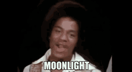 a man in a white shirt is singing a song and the word moonlight is on the screen .