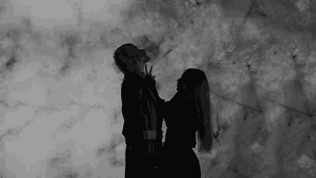 a man and a woman are standing next to each other in front of a marble wall in a black and white photo .
