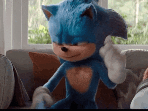 a blue sonic the hedgehog is sitting on a couch giving a thumbs up .