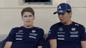 two men wearing williams racing shirts are sitting on a couch