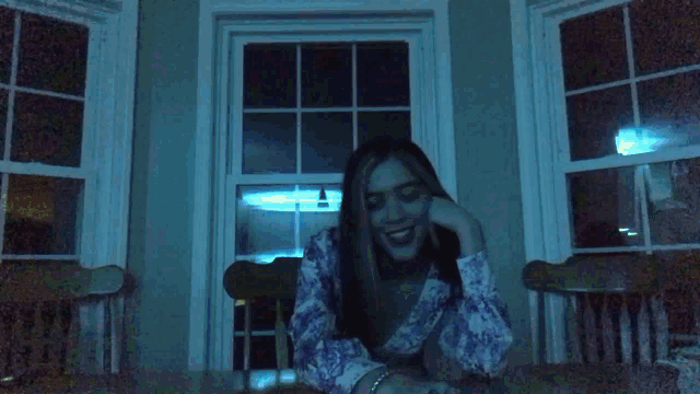 a woman is sitting at a table in front of a window and smiling