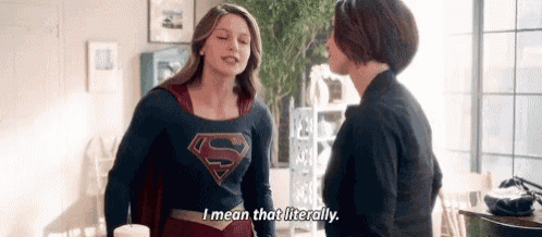 two women in superhero costumes are standing next to each other in a living room and talking .
