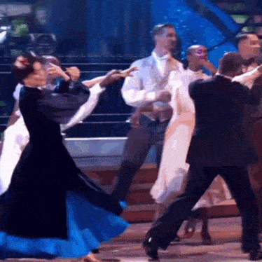 a group of people are dancing on a stage and one woman is wearing a blue dress