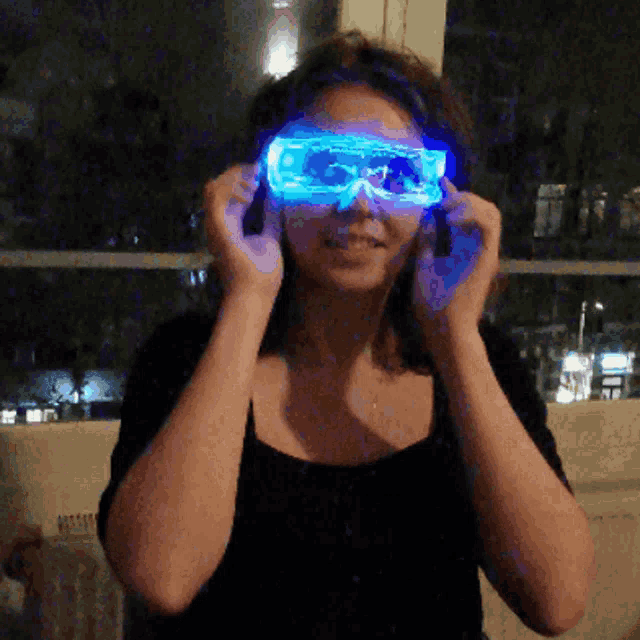 a woman wearing a pair of blue glowing goggles looks at the camera