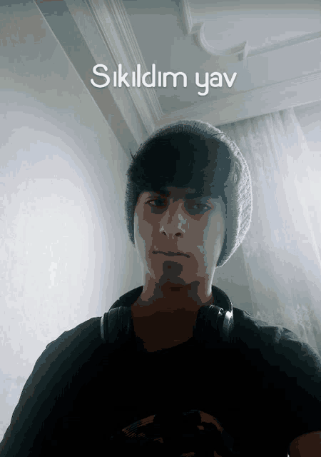 a young man wearing headphones and a beanie stands in front of a wall that says ' sildim yav '