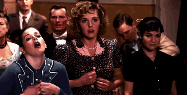 a group of people are standing in a room and one of them is wearing a blue jacket