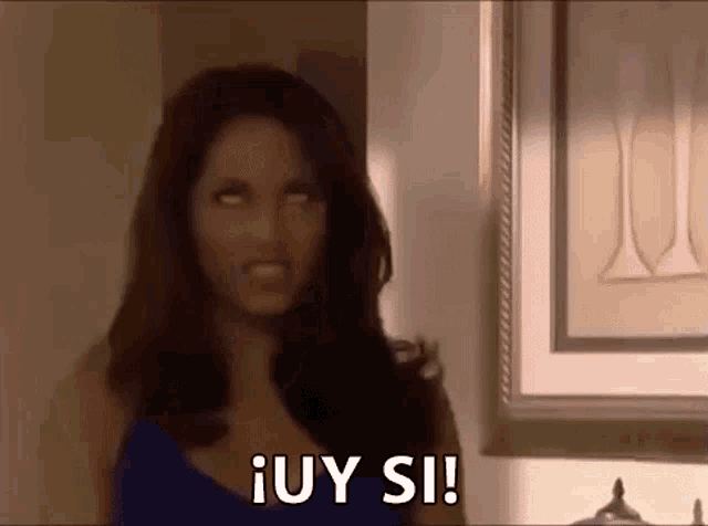 a woman in a blue dress is standing in front of a picture frame and making a face .