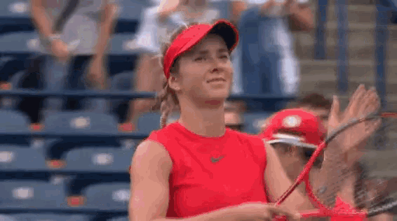 a woman in a red shirt is holding a tennis racquet on a tennis court while a crowd applauds .