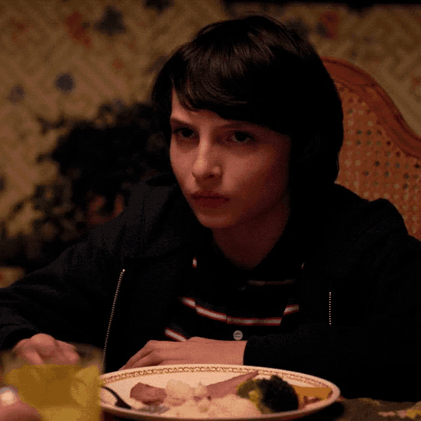 a young boy sits at a table with a plate of food and a glass of orange juice