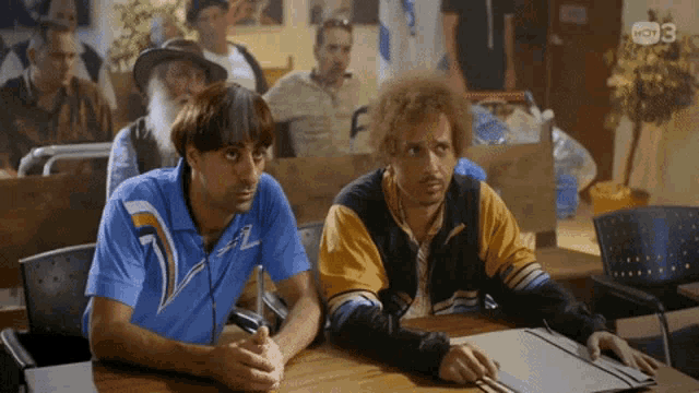 two men sit at a table in front of a sign that says kdv 3