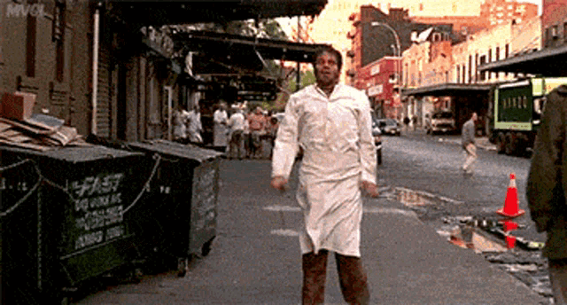 a man in a white apron is walking down a street in front of a green dumpster that says fast