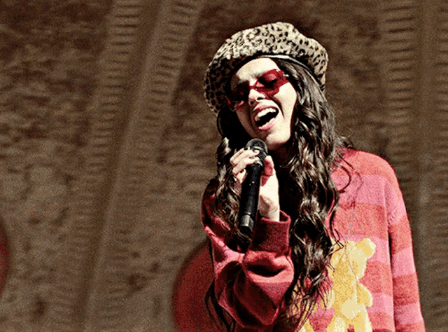 a woman singing into a microphone wearing a leopard hat and sunglasses