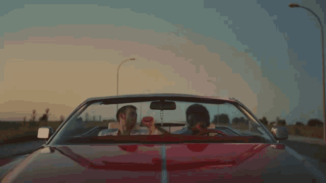 a man and woman are sitting in a red convertible car
