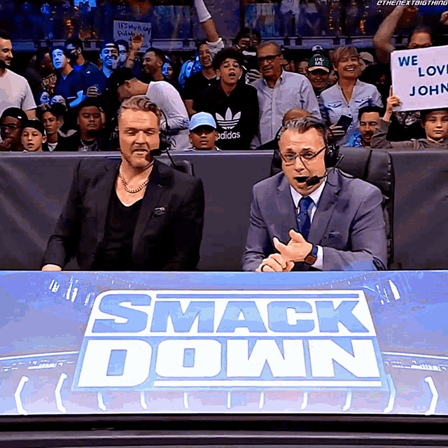 two men sitting at a smack down table with a crowd behind them