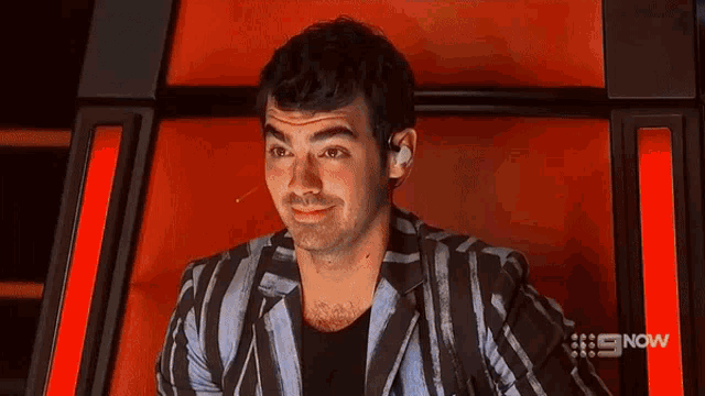a man in a striped jacket is sitting in a chair with a red background .