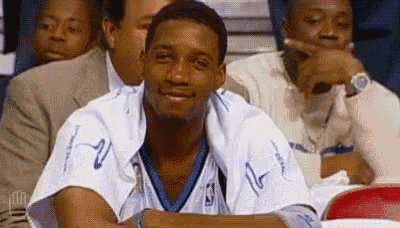 a man in a basketball uniform is sitting in a stadium with other people .