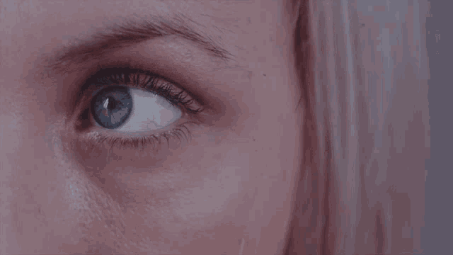 a close up of a woman 's blue eye with a pink background