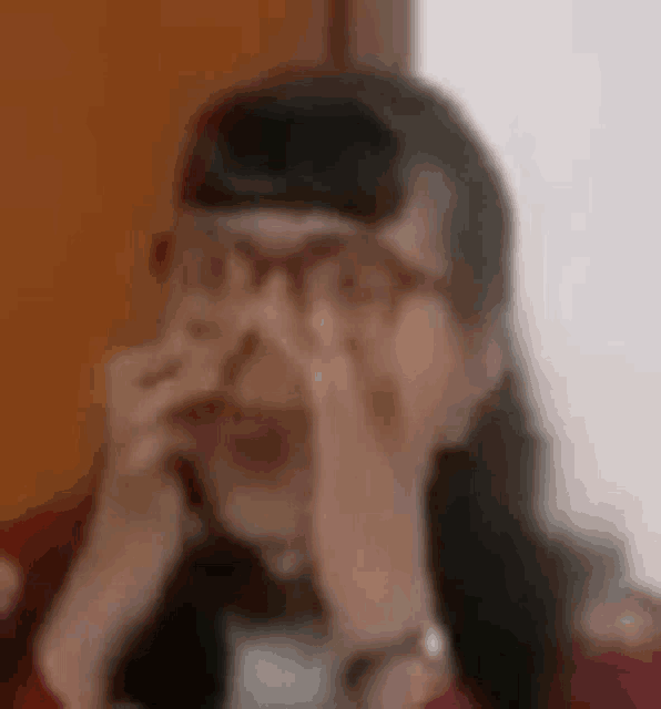a close up of a woman wearing glasses covering her nose with her hands .