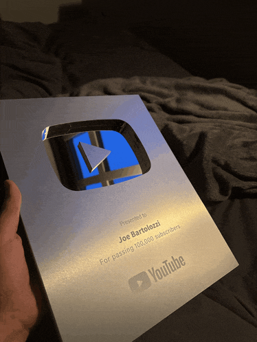 a person is holding a youtube plaque in front of a bed