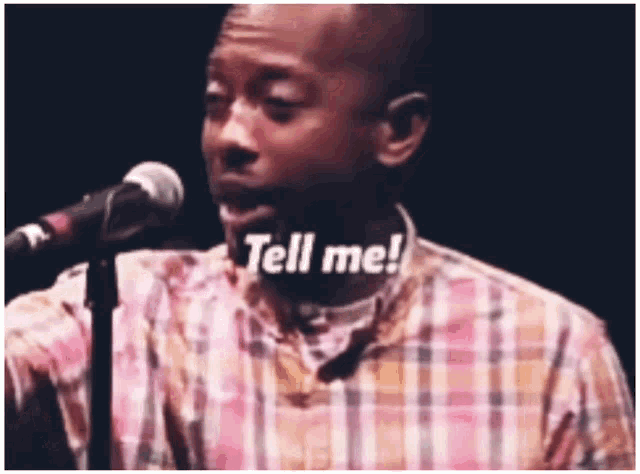 a man in a plaid shirt is singing into a microphone and the words tell me are on his face