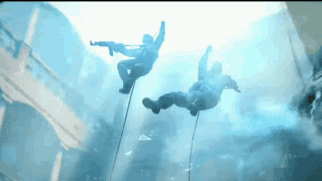 two soldiers are hanging from ropes in the water .