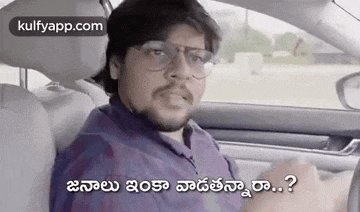 a man is sitting in the driver 's seat of a car with a beard and glasses .
