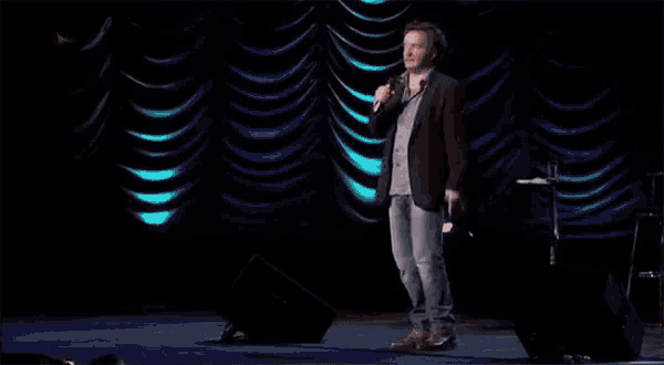 a man stands on a stage holding a microphone in front of a blue curtain