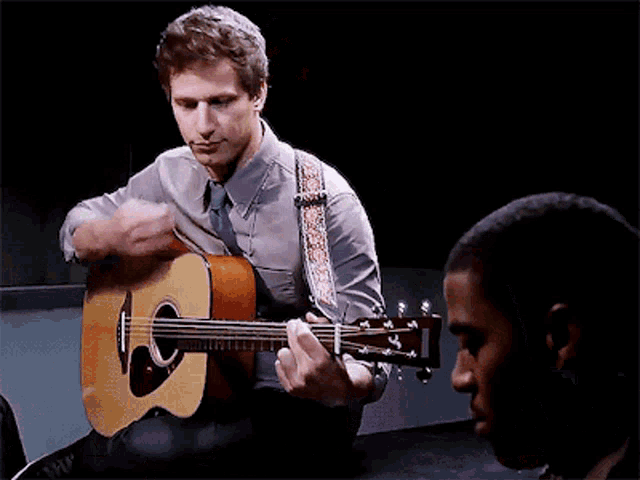 a man playing an acoustic guitar next to a man with the word aaaa on the bottom right