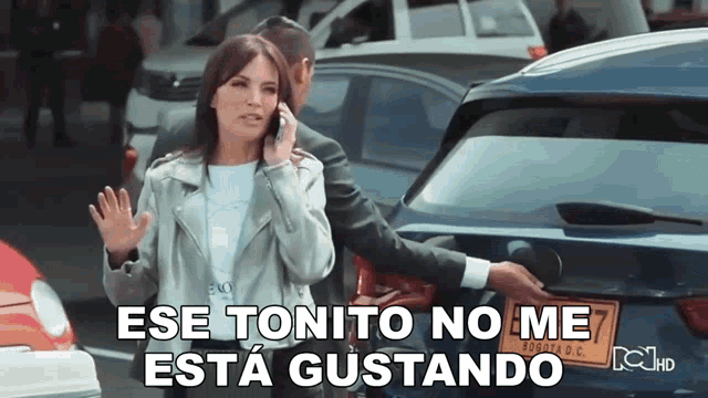 a woman talking on a cell phone next to a man standing next to a car that says ese tonito no me