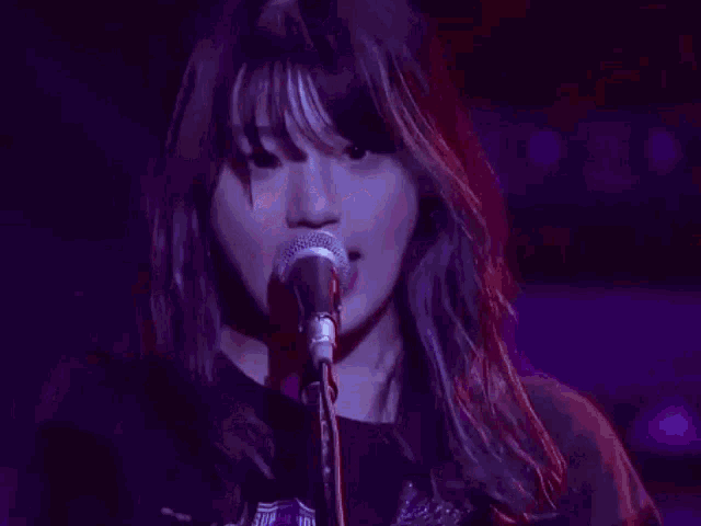 a woman is singing into a microphone in a dark room and pointing at the camera .
