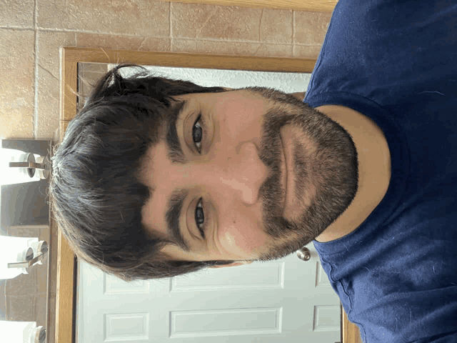 a man with a beard wearing a blue shirt is smiling