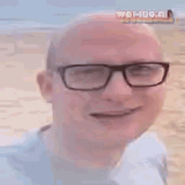a bald man wearing glasses and a blue shirt is smiling on the beach .