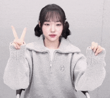 a girl wearing a grey sweater with the letter r on it makes a peace sign