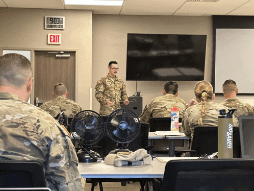 a man in a military uniform stands in front of a group of soldiers in a classroom
