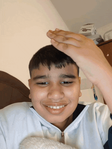 a young boy is smiling and holding his hand up to his forehead