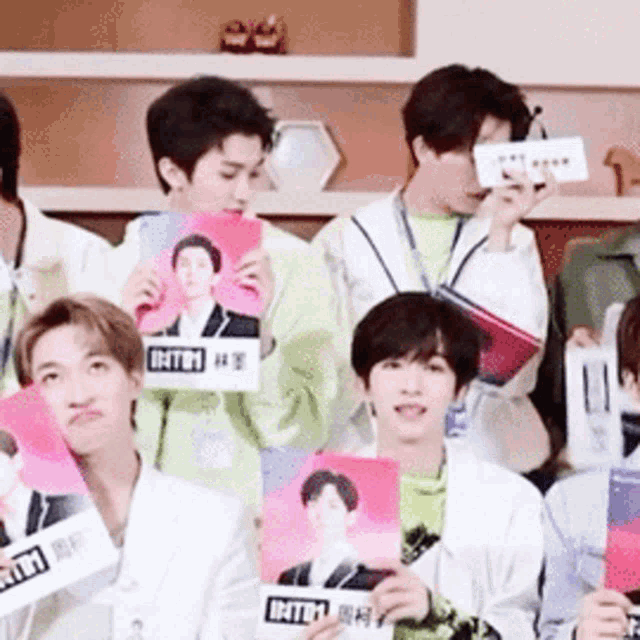 a group of young men are sitting in a room holding cards with pictures of themselves on them .