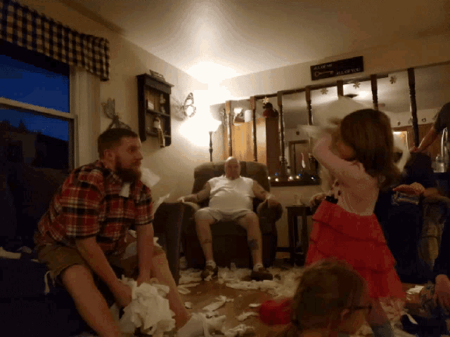 a man sits in a chair in a living room surrounded by a bunch of toilet paper
