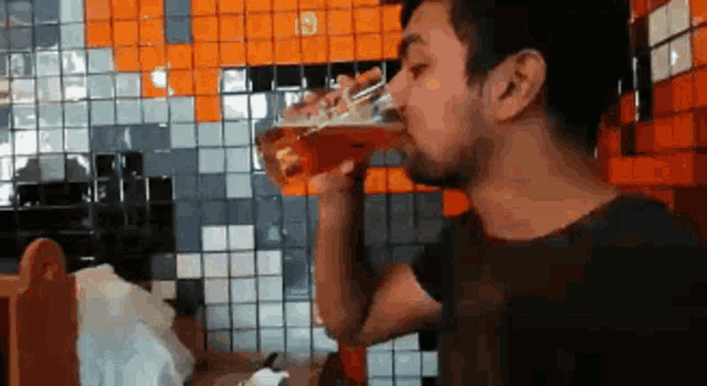 a man is drinking a glass of beer in front of a tiled wall ..
