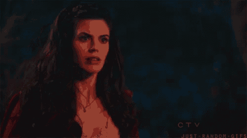 a woman in a red cape is standing in the dark looking at something .