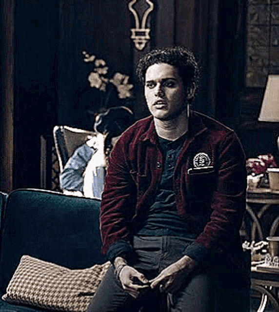 a man in a red jacket is sitting on a blue couch holding a cup of coffee .