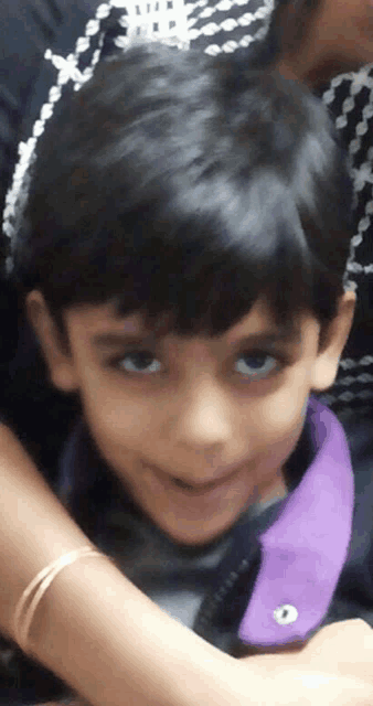 a young boy wearing a purple jacket is smiling