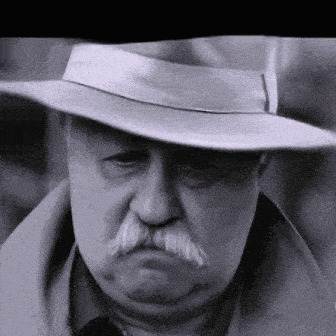 a man with a mustache wearing a hat and a trench coat