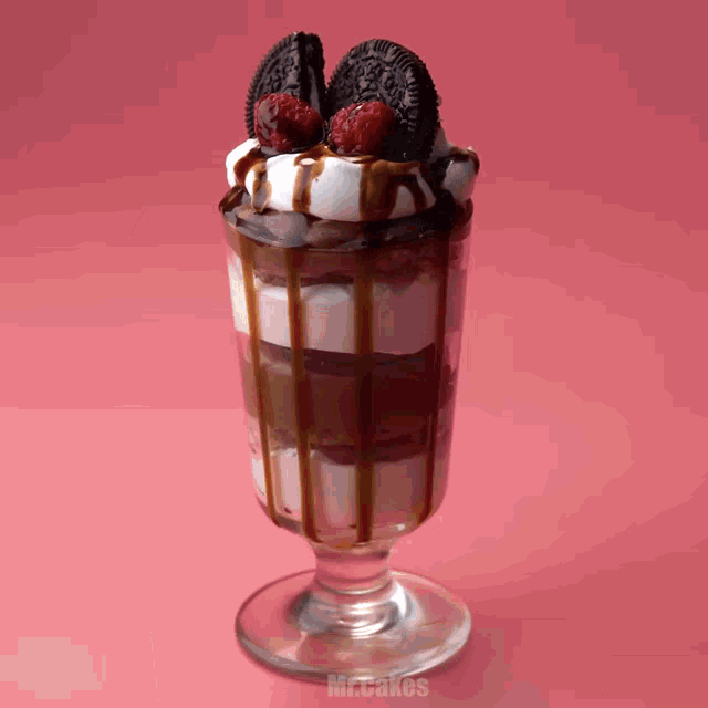 a sundae with oreos and raspberries in a glass on a pink background